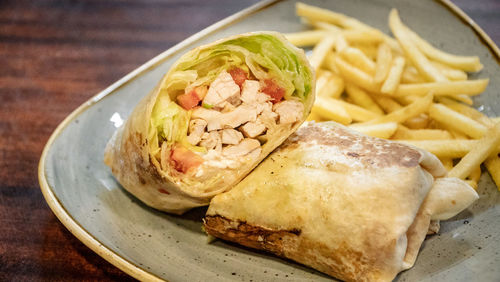 A tasty image of a freshly prepared chicken tortilla wrap filled with salad and served with fries