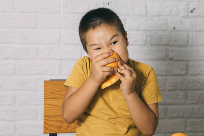 A curious asian boy in a yellow t-shirt enjoys a juicy orange, the concept and benefits of vitamin c