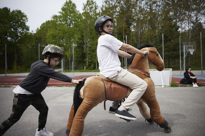 Boys having fun riding horse on wheels outdoors