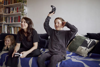 Mother with sons sitting on sofa and playing video games