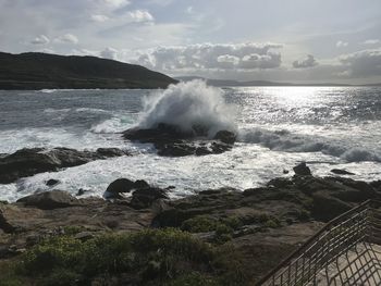 Waves splashing on rocks at shore against sky