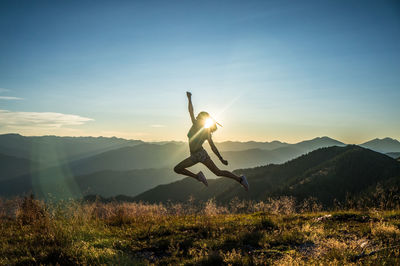 Woman jumping on mountain against sky during sunset