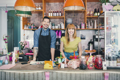 Portrait of male and female baristas standing at cafe counter