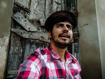 Man wearing hat looking away against old house 