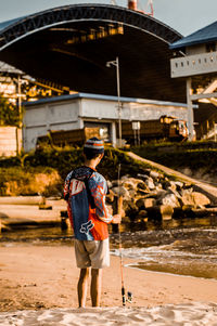 Rear view fisherman holding fishing rod while standing outdoors