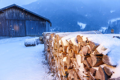 Stack of logs on snow covered field by building