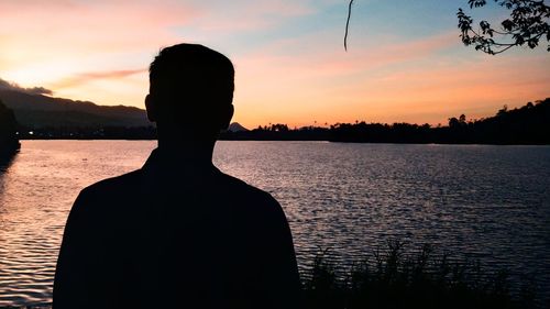 Silhouette man by lake against sky during sunset