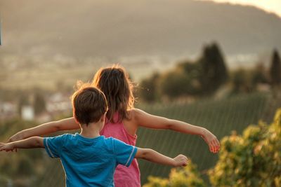 Rear view of siblings with arms outstretched standing on field