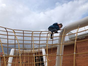 Low angle view of girl playing on outdoor play equipment against cloudy sky