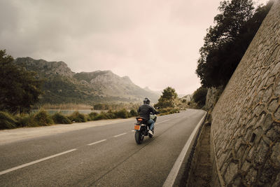 Man riding motorcycle on road in front of mountains aganist sky