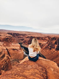 Rear view of woman sitting on rock formation against sky