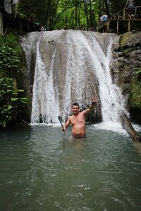 Man showing peace sign in river against waterfall