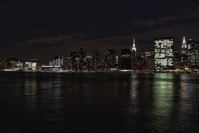 Illuminated buildings by river against sky at night