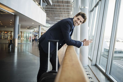 Side view of happy businessman leaning on railing at airport