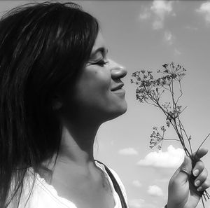 Close-up of beautiful woman holding flower against sky