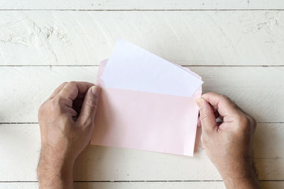 Directly above shot of cropped hands holding envelope at table