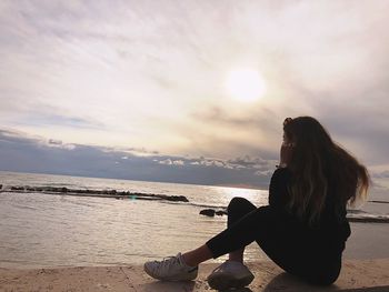 Woman sitting on beach against sky during sunset