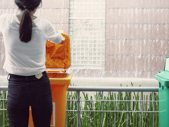 Rear view of woman standing against recycling bin and railing