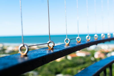 Close-up of chain hanging on railing by sea against clear sky
