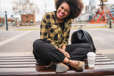 Smiling young woman sitting on sidewalk in city