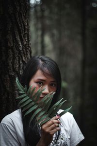 Portrait of happy girl holding tree trunk in forest