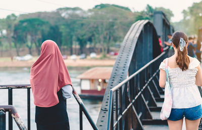 Rear view of women standing on railing against bridge