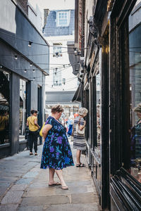 Rear view of woman walking on footpath amidst buildings in city