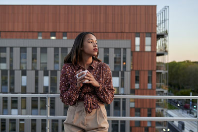 Thoughtful young woman having coffee in balcony at sunset