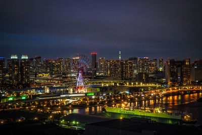 Illuminated buildings by river against sky at night