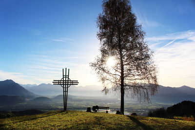 Cross shaped metal and tree on field against sky