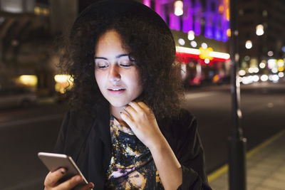 Woman using smart phone sidewalk in city at night