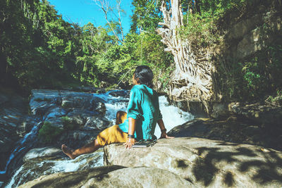 Rear view of man sitting on rock in forest