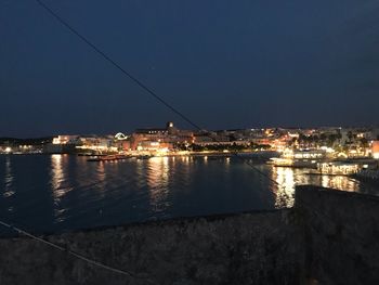 Illuminated buildings by sea against clear sky at night