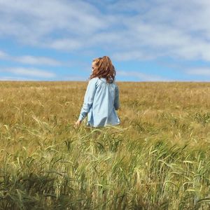 Rear view of woman standing on wheat field against sky