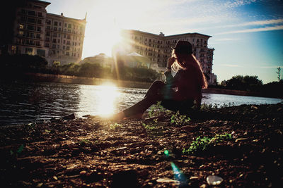 Man sitting in city against sky during sunset