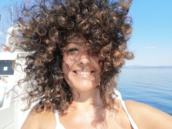 Close-up portrait of smiling woman with tousled hair against sea