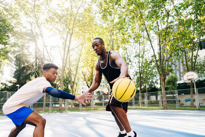 Ethnic african american friends players running together with ball while playing basketball on sports ground in sunny day