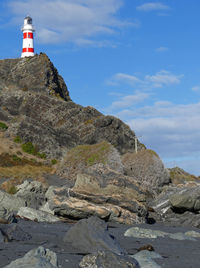 Low angle view of lighthouse on cliff by sea against sky