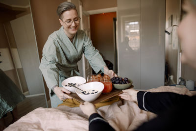 Lesbian woman serving breakfast in bed to girlfriend at home