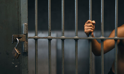 Midsection of prisoner holding railing while standing in prison