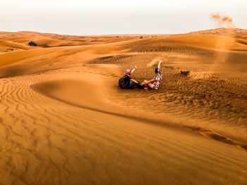 People sitting on sand dune in desert against sky