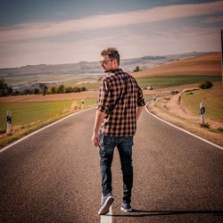 Rear view of man walking on road against sky