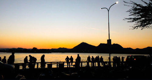 Silhouette people at lakeshore against sky during sunset