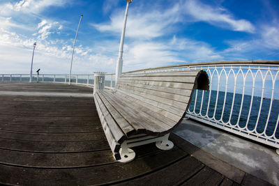 Fish-eye lens view of empty bench at observation point against sky