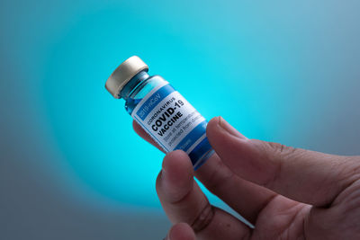 Close-up of hand holding bottle against blue background