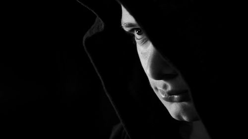 Close-up of man in hood clothing against black background