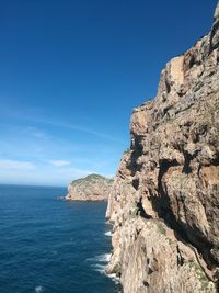 Rock formation in sea against clear blue sky