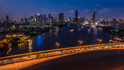 Illuminated city by river against sky at night