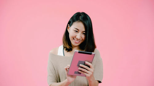 Portrait of woman using mobile phone against pink background