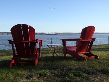 Empty red chairs by lake against clear sky